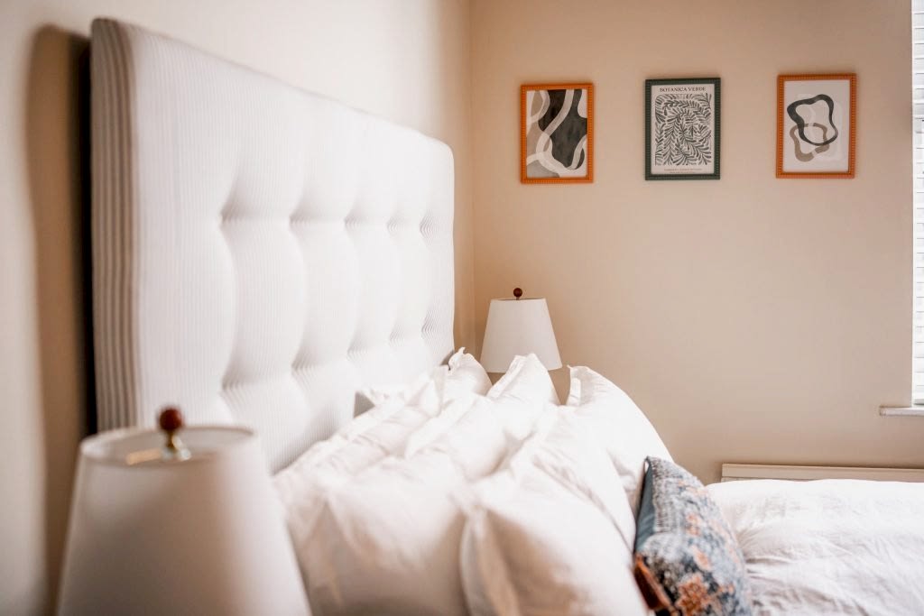 This inviting bedroom corner in an Anfield, Liverpool serviced accommodation showcases a plush, tufted white headboard paired with crisp white linens for a luxurious sleep experience. Above...