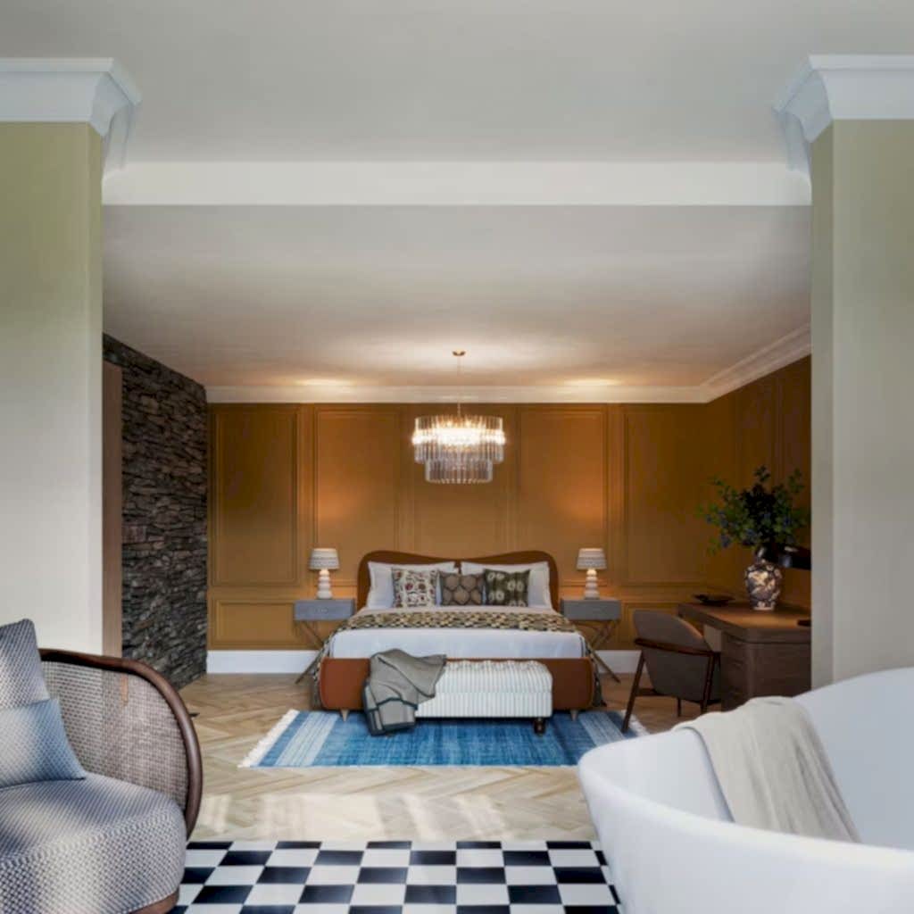 Expansive suite with panelled walls, a stone-clad recess and a freestanding bath, anchored by a glass chandelier.