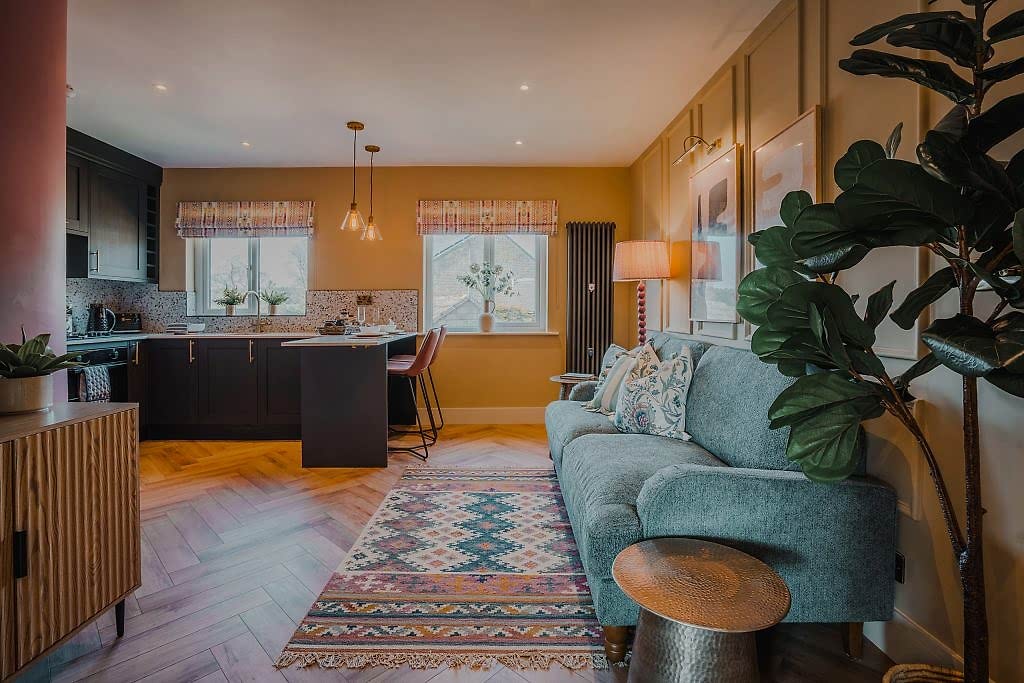Discover a beautifully designed serviced accommodation in Beckwithshaw, North Yorkshire featuring an open-plan living area with mustard-yellow paneled walls, a sleek black kitchen island...