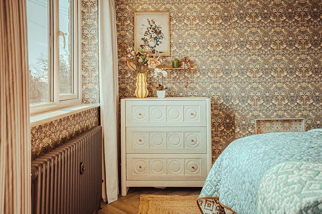 Discover this cozy serviced accommodation in Beckwithshaw, North Yorkshire, featuring an inviting bedroom corner with intricate floral-patterned wallpaper, a white vintage dresser...