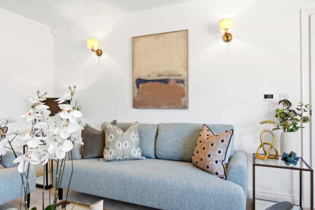 Living room with a blue sofa, brass wall lights, a gold-accented side table and a calm abstract print.