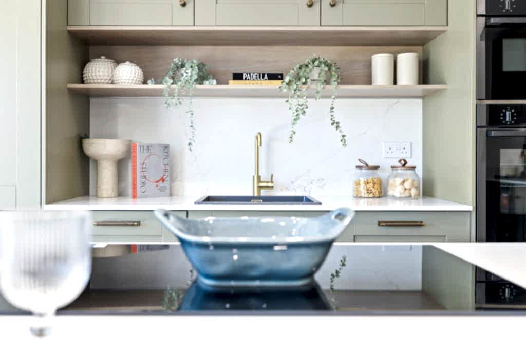 Kitchen with sage and cream cabinetry, a brushed-gold tap, open shelving and softly styled worktops.