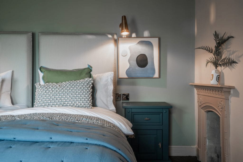 A tranquil bedroom detail in Magazine Lane serviced accommodation, The Wirral, styled by WildKind Interiors. This vignette features twin striped upholstered headboards with coordinating...