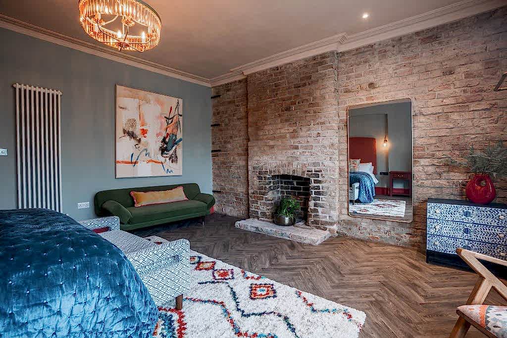Living room with an exposed brick fireplace, an emerald green sofa and a characterful bay window.
