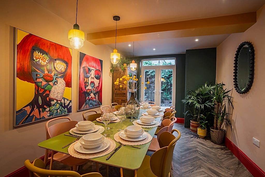 Dining room with a pastel-green table, mismatched colourful chairs and bold pop-art on the walls.
