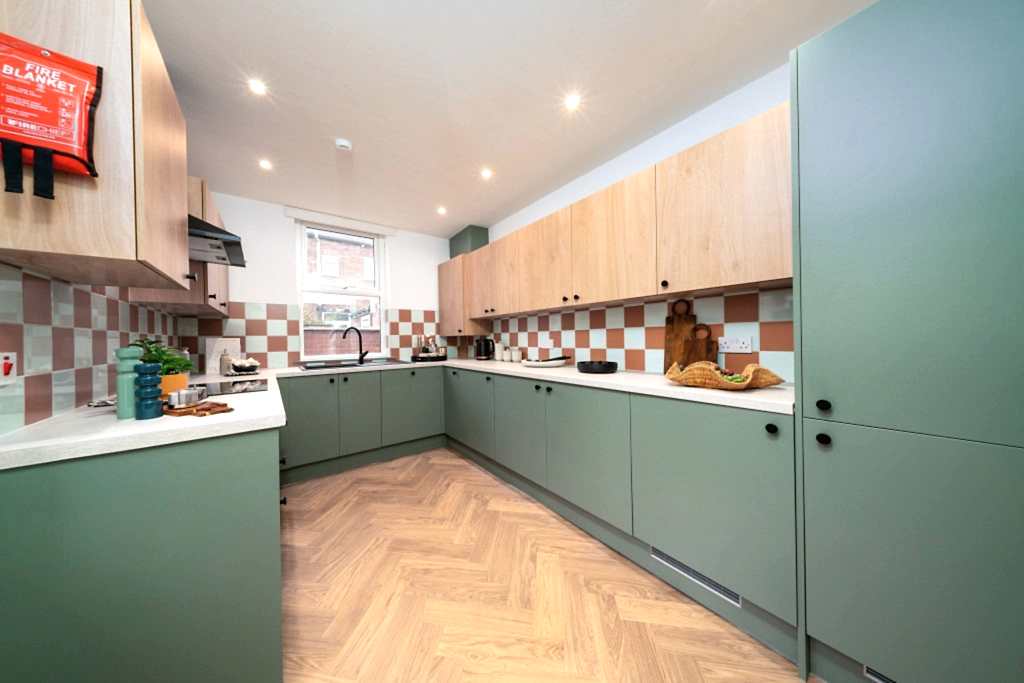 Communal kitchen with sage-green cabinetry, oak uppers, a checkerboard splashback and herringbone flooring.