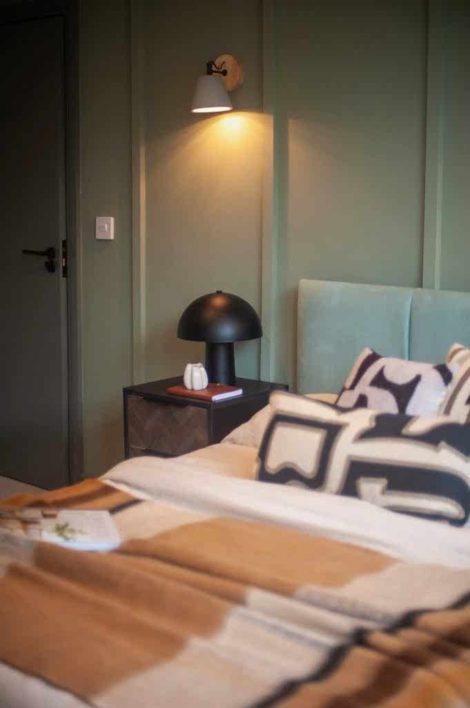 Tenant bedroom with a sage-green panelled wall, teal headboard and a timber bedside table.