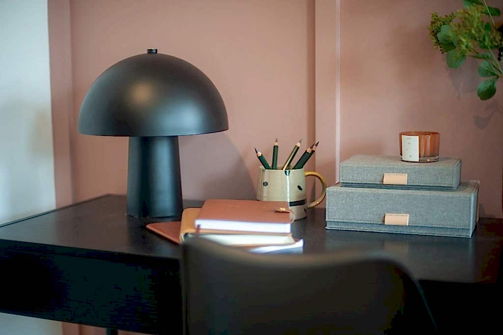 Styled desk detail with a domed lamp, candle and greenery against a blush feature wall.