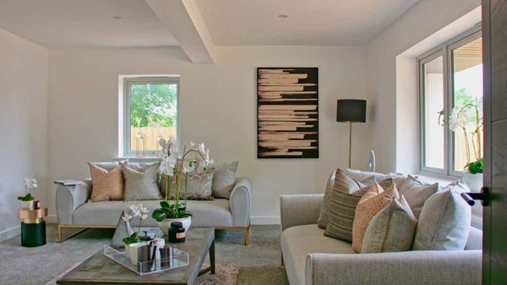 Living room with two pale sofas, orchids on a mirrored coffee table and a bold monochrome artwork between bright garden windows.