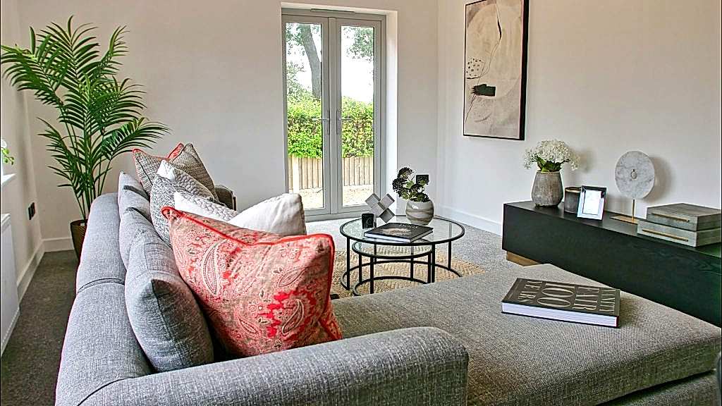 Living room detail with a coral paisley cushion layered on a grey sofa, a round glass coffee table and a tall palm by the French doors.