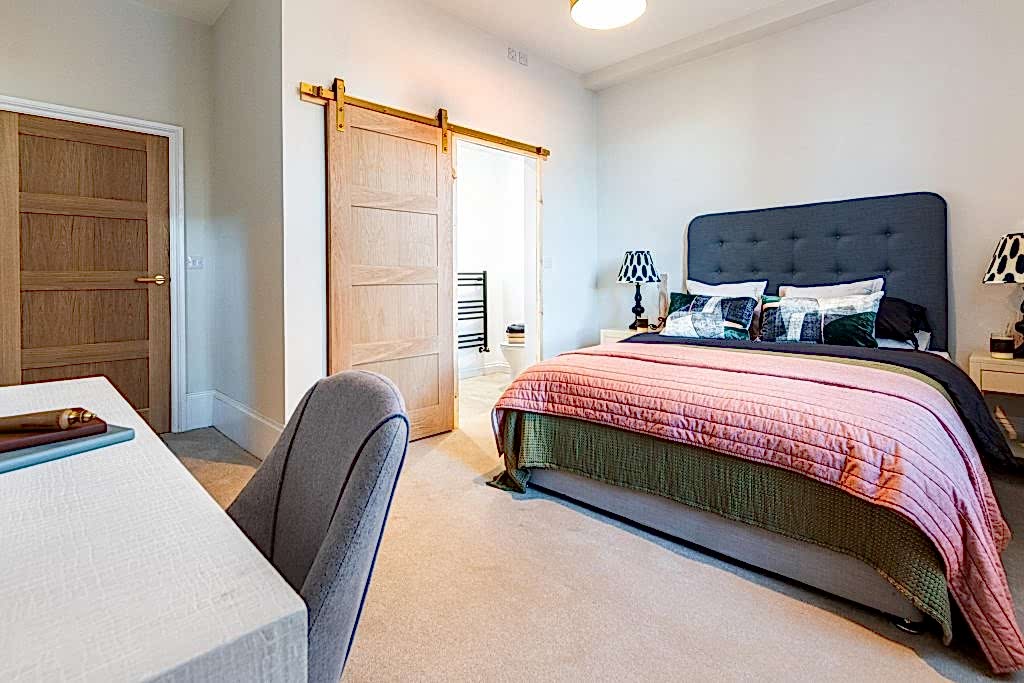 This expertly staged master bedroom in Scartho, Lincolnshire features a contemporary grey upholstered headboard bed dressed in layered bedding: an olive-green quilt topped with a dusty-rose...