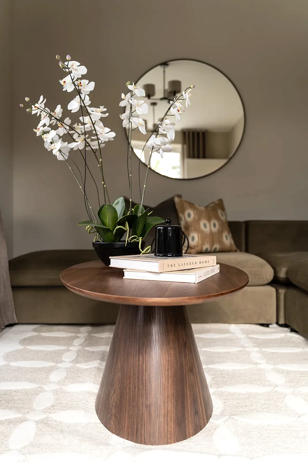 Walnut pedestal table with orchids and books in a styled show home living room